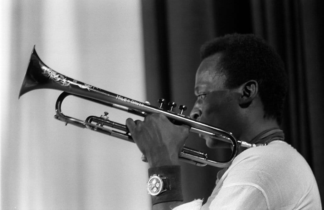 Miles Davis playing trumpet on stage wearing a Breitling Navitimer watch, captured in black and white — a portrait of precision, rhythm, and timeless cool.