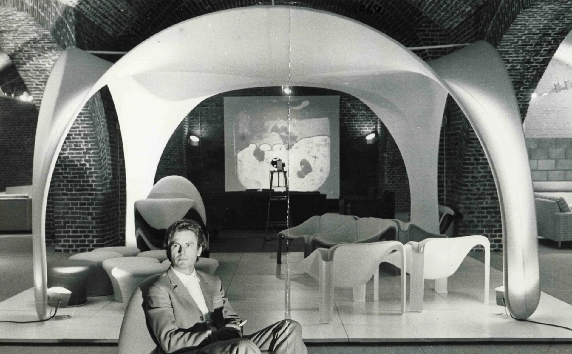 Archival photograph of designer Pierre Paulin seated beneath his futuristic white dome installation, surrounded by his sculptural furniture.