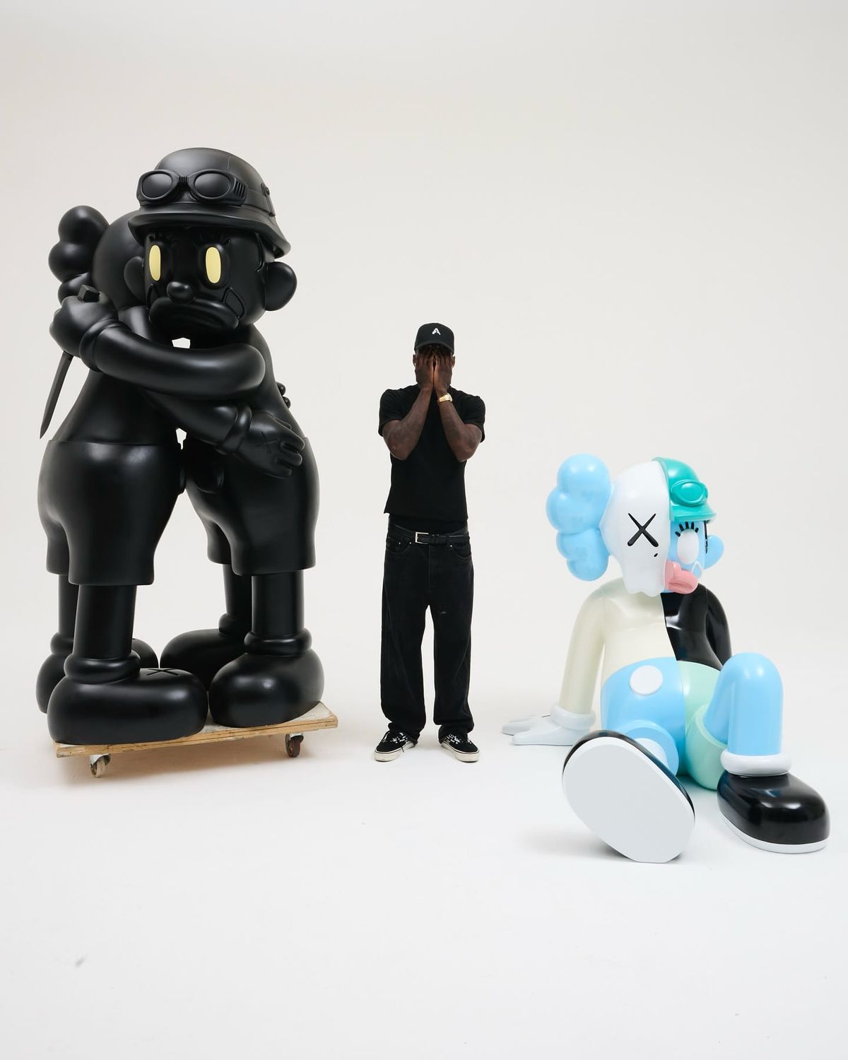 Olaolu Slawn standing between large black and pastel sculptures in a white gallery space, captured in a moment of reflection between playfulness and scal