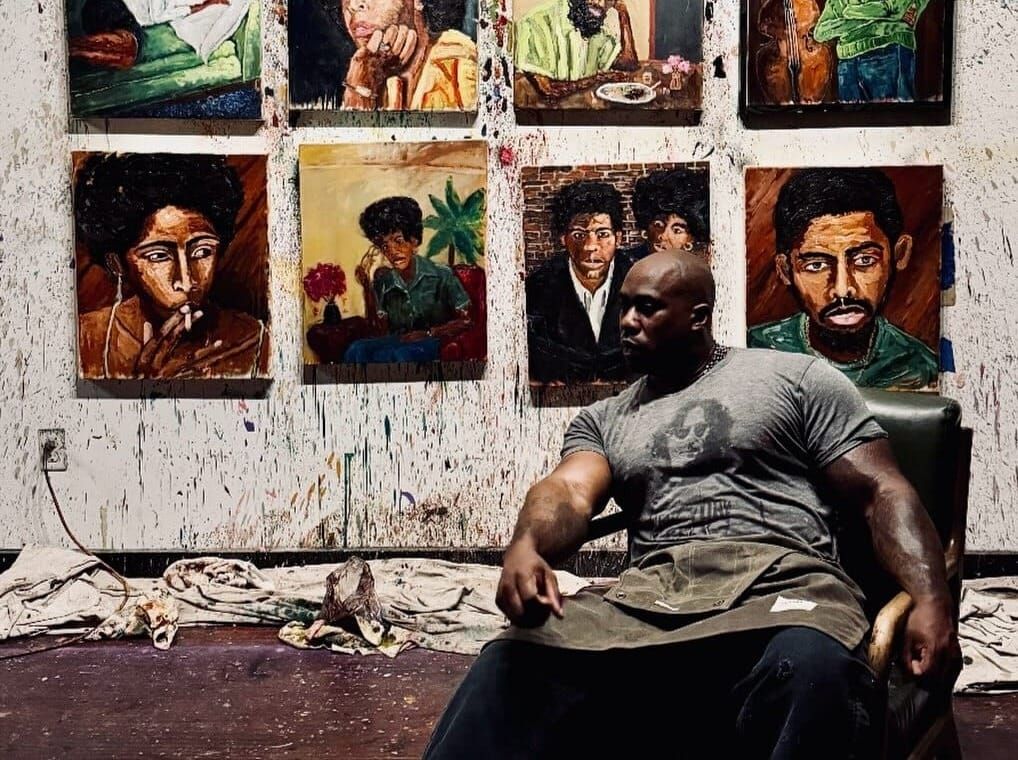 Ronnie Robinson sitting in an armchair in front of his paintings.