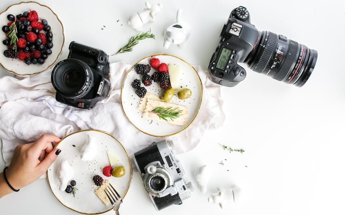 three assorted cameras near fruits and ceramic figurines