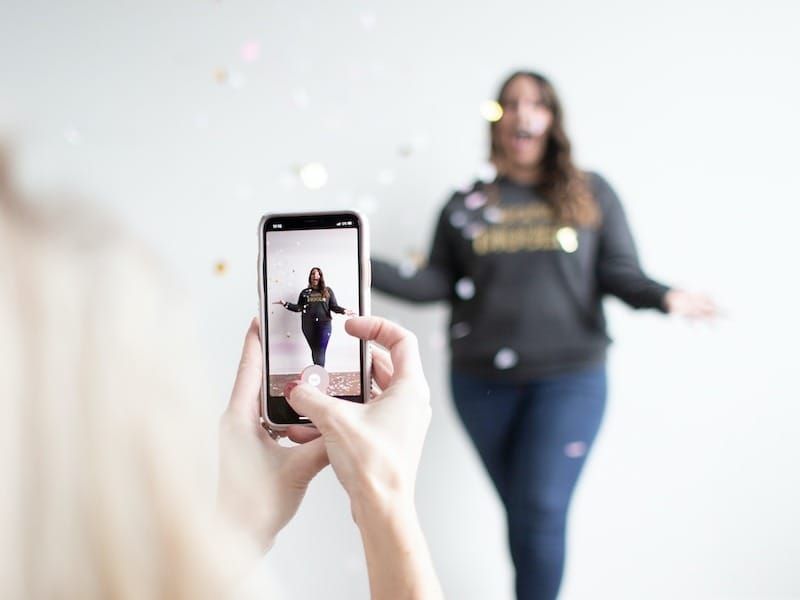 person holding white smartphone taking photo of woman wearing blue jeans