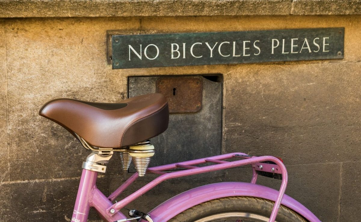 A pink bicycle leaned up against a wall with the sign "No Bicycles Please"