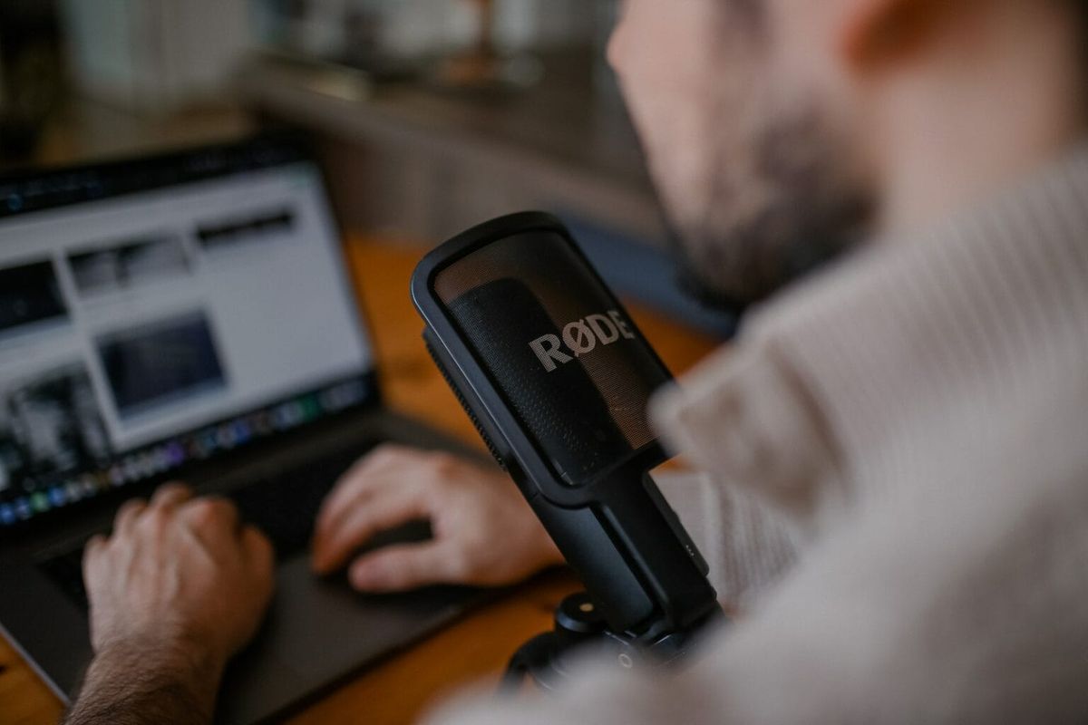 A man typing on a laptop while speaking into a RODE microphone