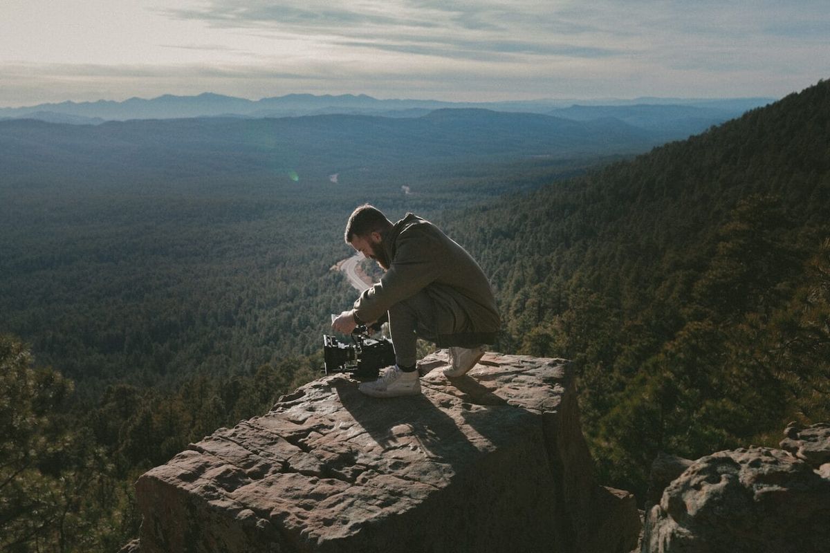 Man crouching on top of mountain with a DSLR camera