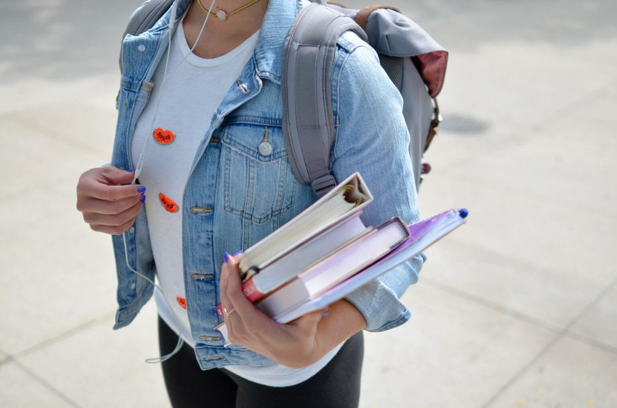 A student wearing a backpack and holding onto several books