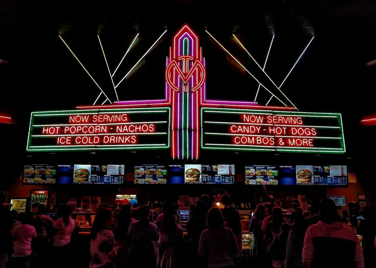 A shot of people lined up in front of a concession stand at a movie theatre.