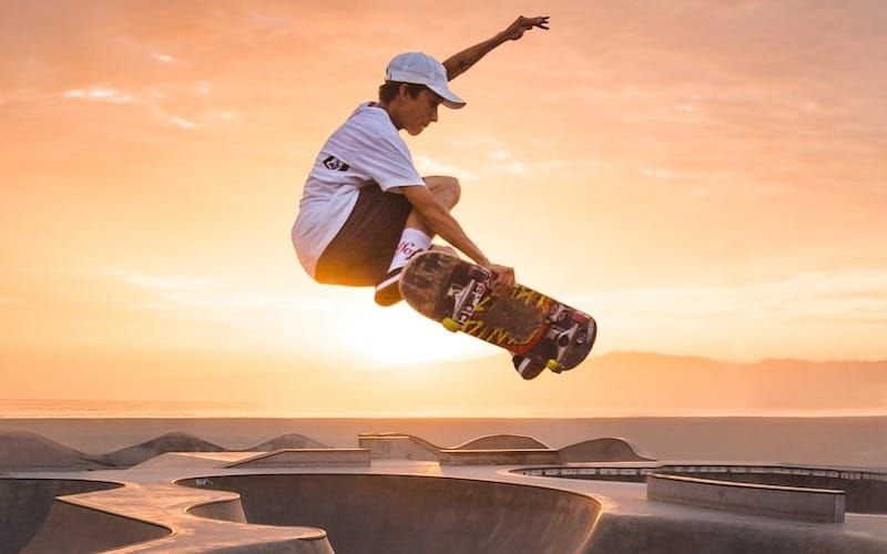 man in white t-shirt and brown pants riding skateboard on brown sand during daytime
