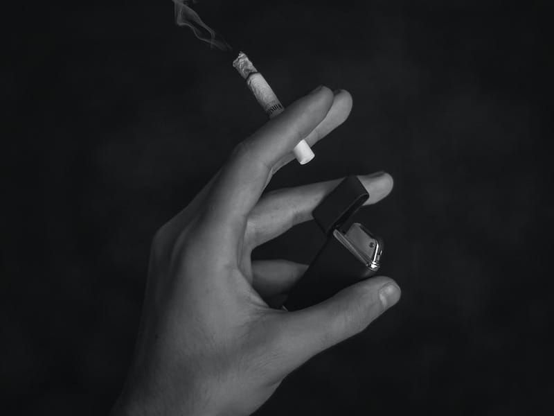 grayscale photo of person holding cigarette stick