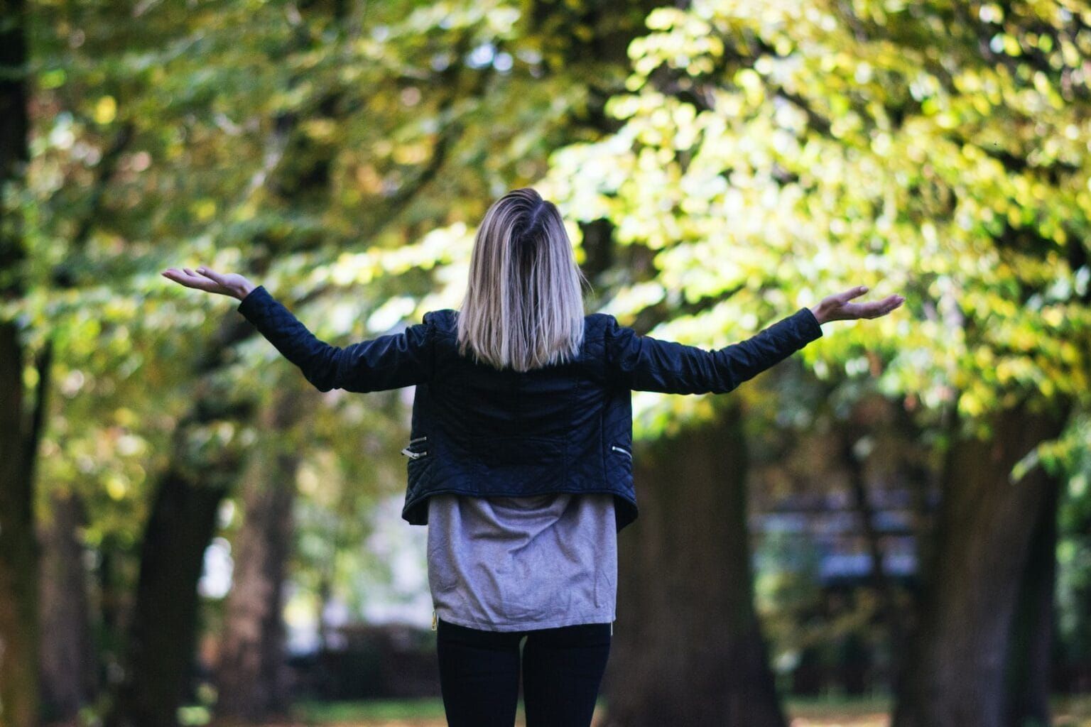 A woman with a black long-sleeved shirt against a backdrop of tall trees