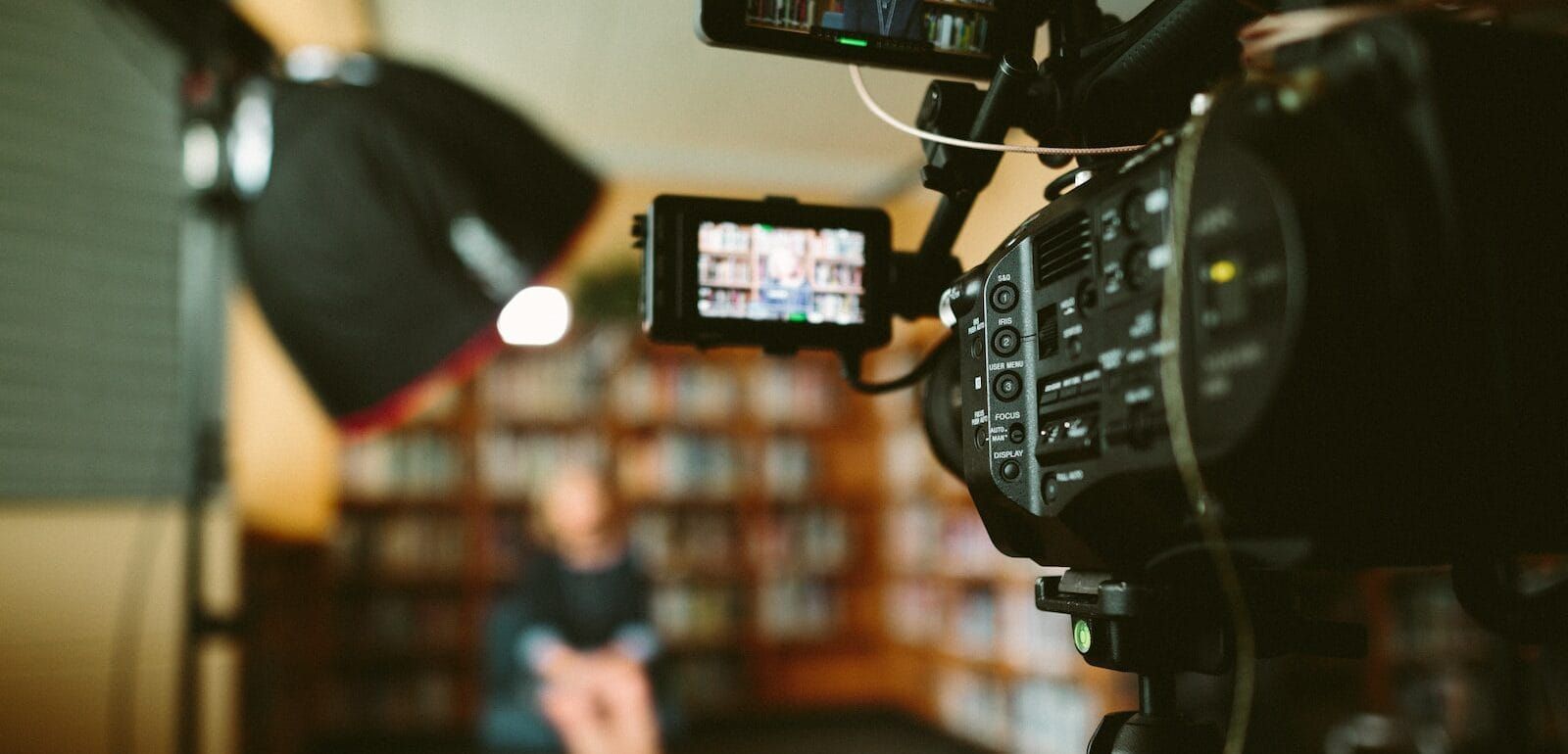 A video camera pointed at an individual sitting in front of a bookshelf