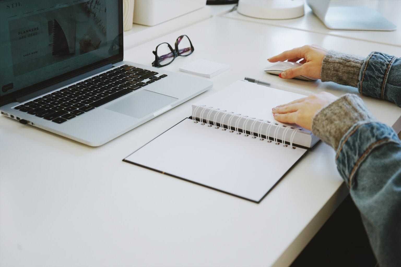 An individual scrolling through the laptop and using a notebook
