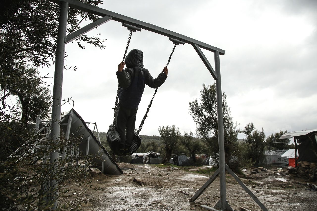 Дете в гръб, което се люлее на импровизираната люлка в лагера „Мория“