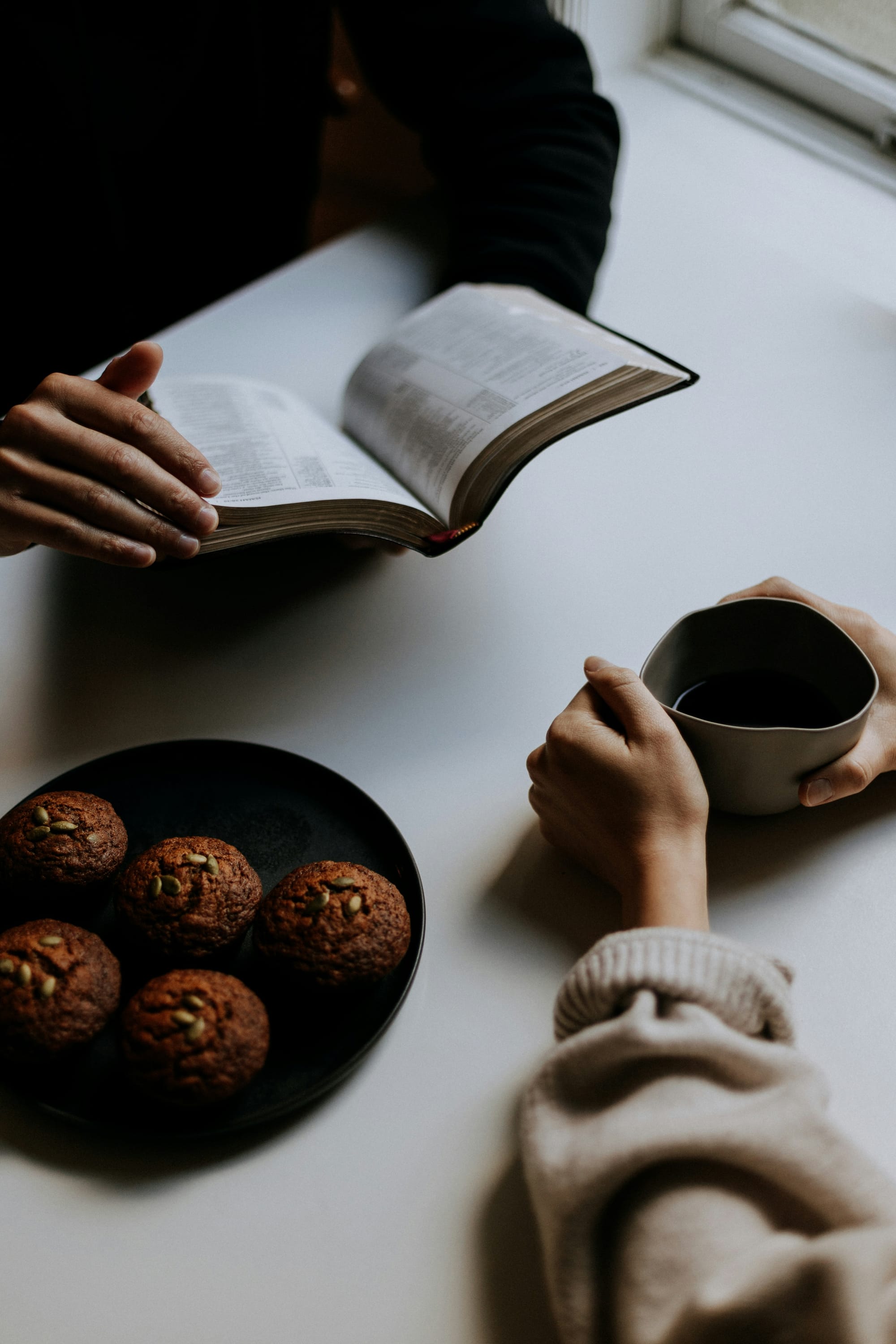 A couple have coffee together with a plate of cookies in between them