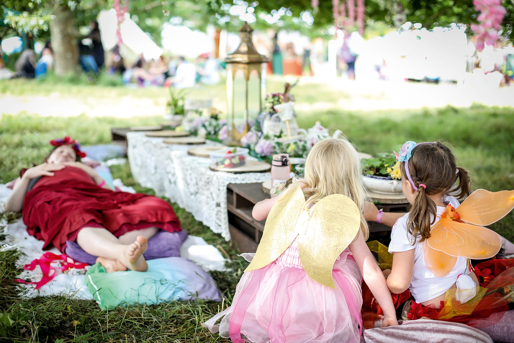 Image shows a table laid with fairy and flowery treats, mother resting alongside and two children dressed as fairies