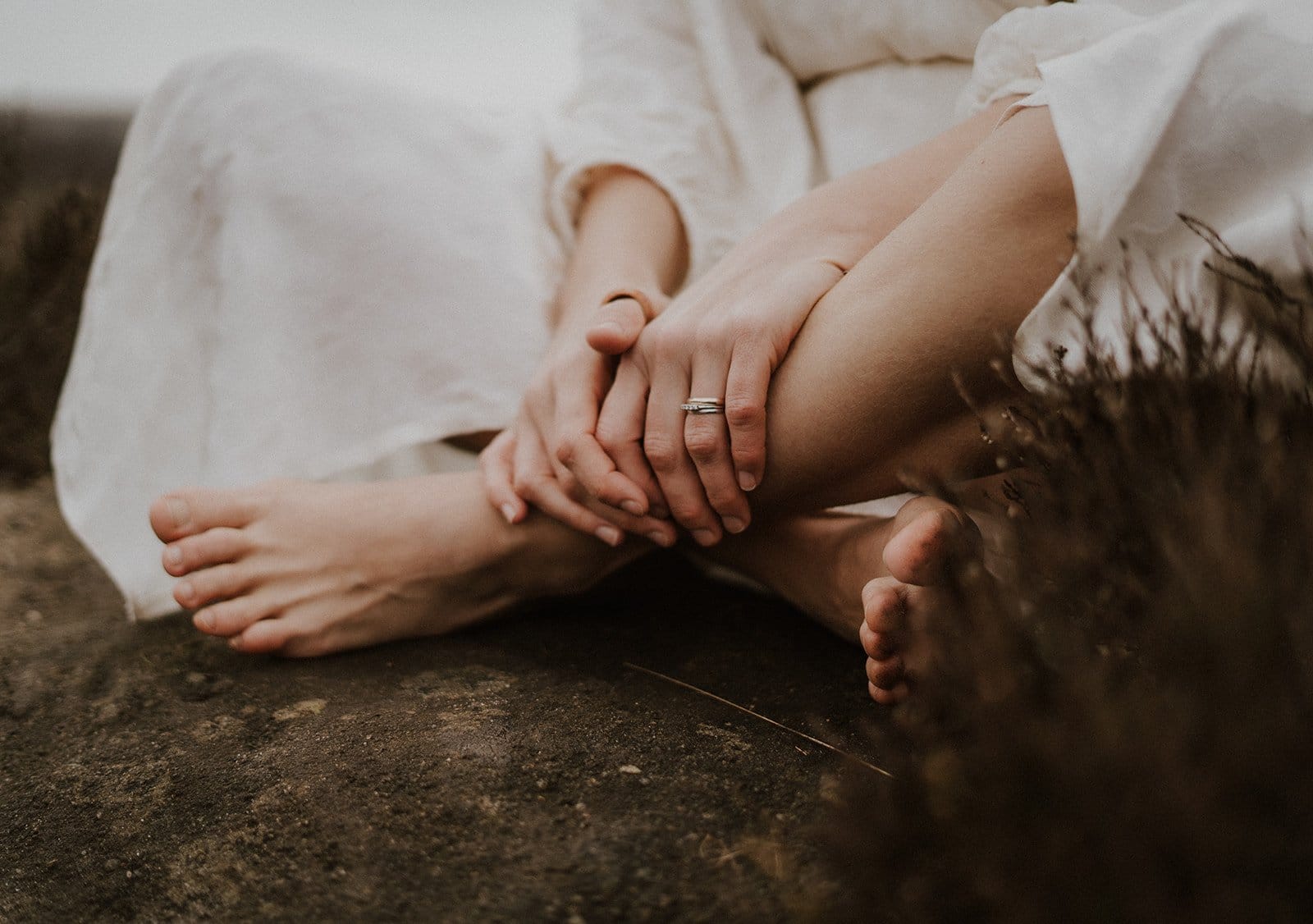 Photograph of a woman's legs sitting on a rock, crosslegged and wearing a white dress