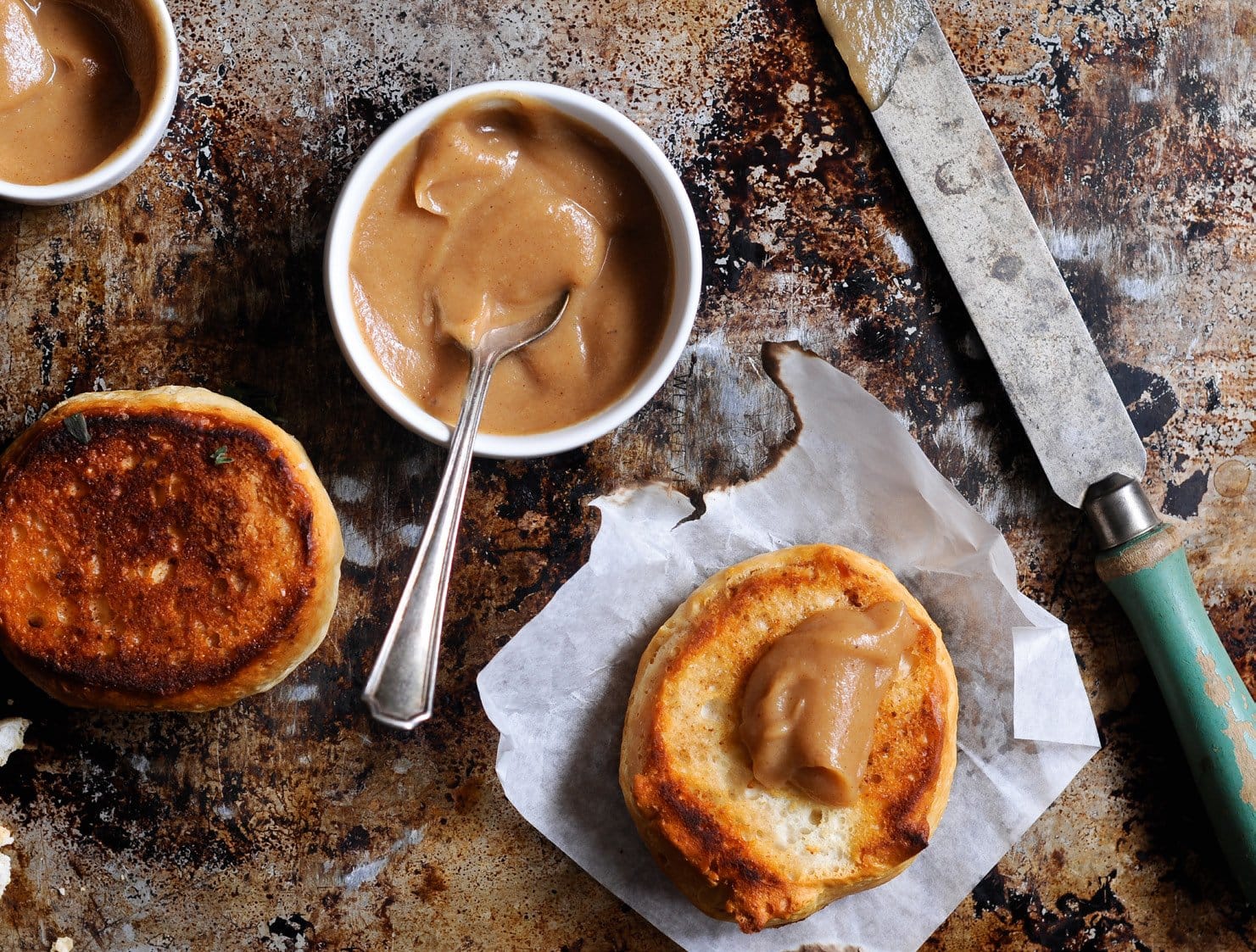 A jar of smooth, caramel-coloured apple butter beside toast and fresh apples on a wooden board