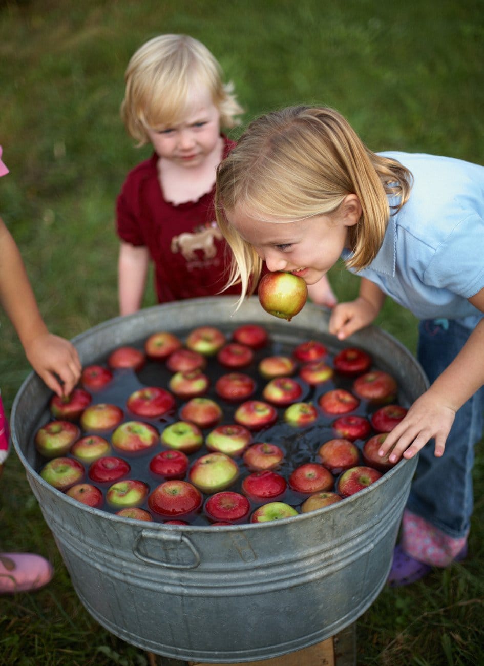 Two young children lean over a tin bath full of red and green apples floating in water