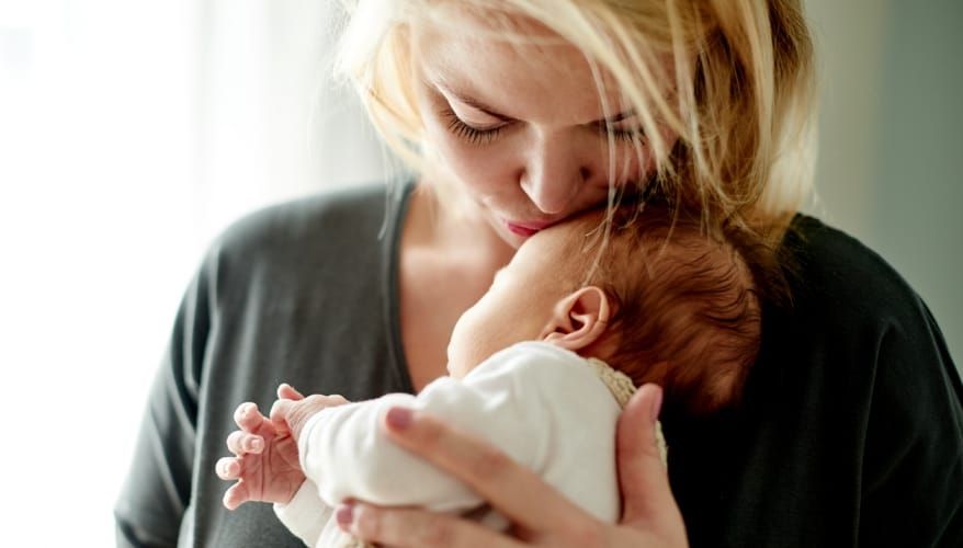 Mother holding tiny newborn and kissing their head