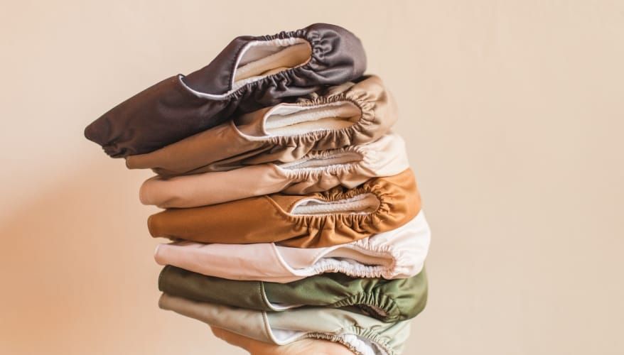 Photo of a hand with a pile of washable nappies in muted colours resting on top.
