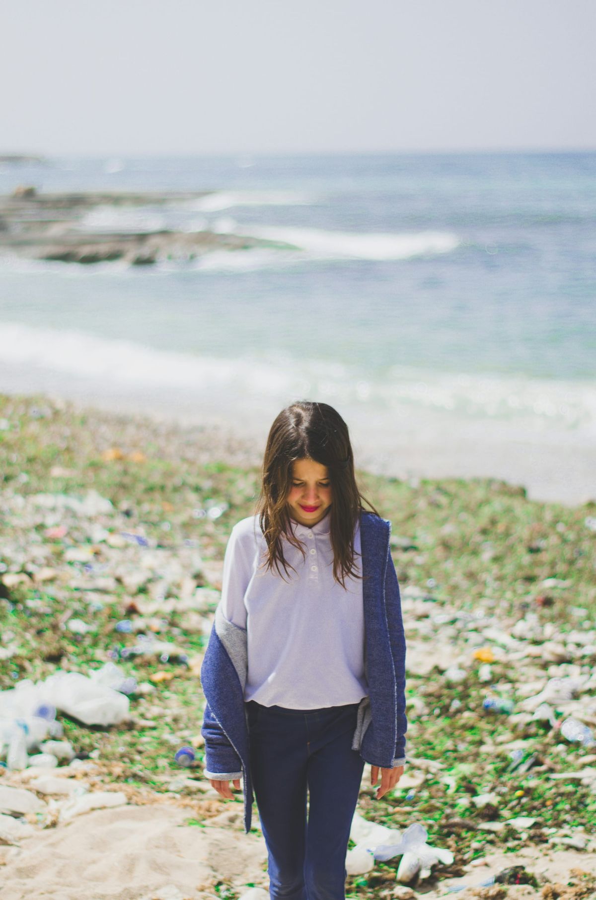 A child stands on a shoreline looking down at the ground.