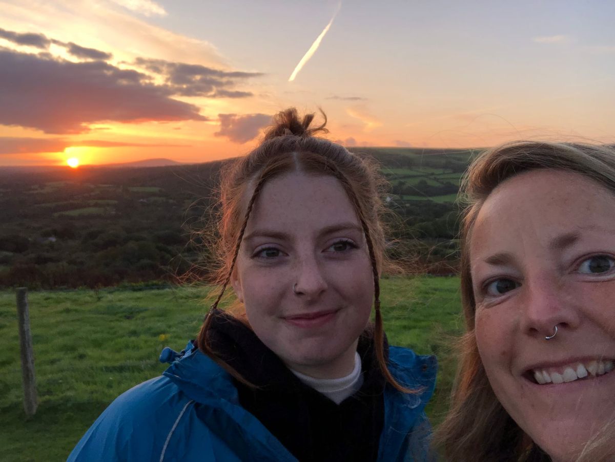 Photograph of a mother and her daughter on Mynydd Carningli at sunrise, with sun glowing orange in background