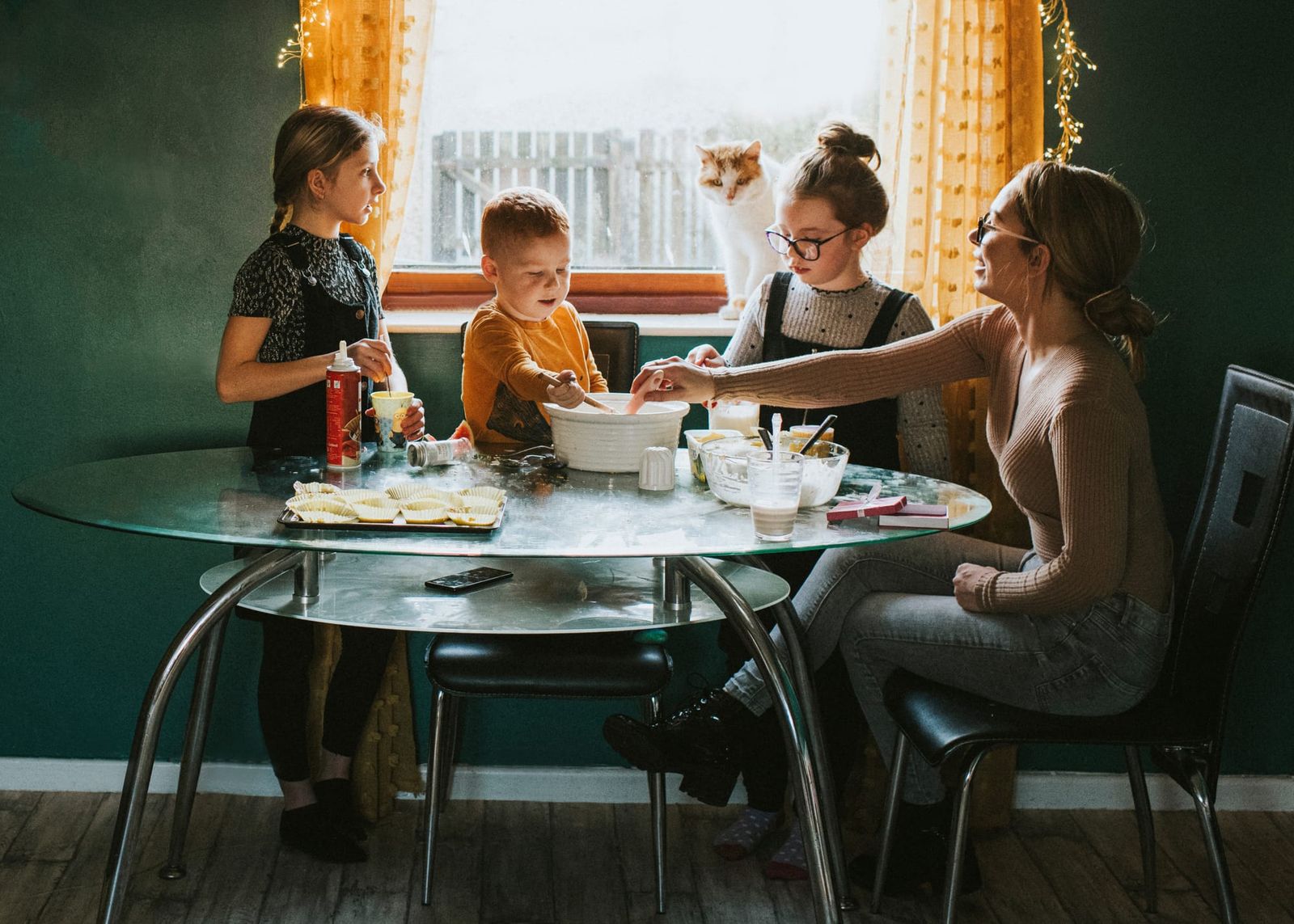 Photograph of an unschooling family sitting around a table baking together, overlooked by the family cat