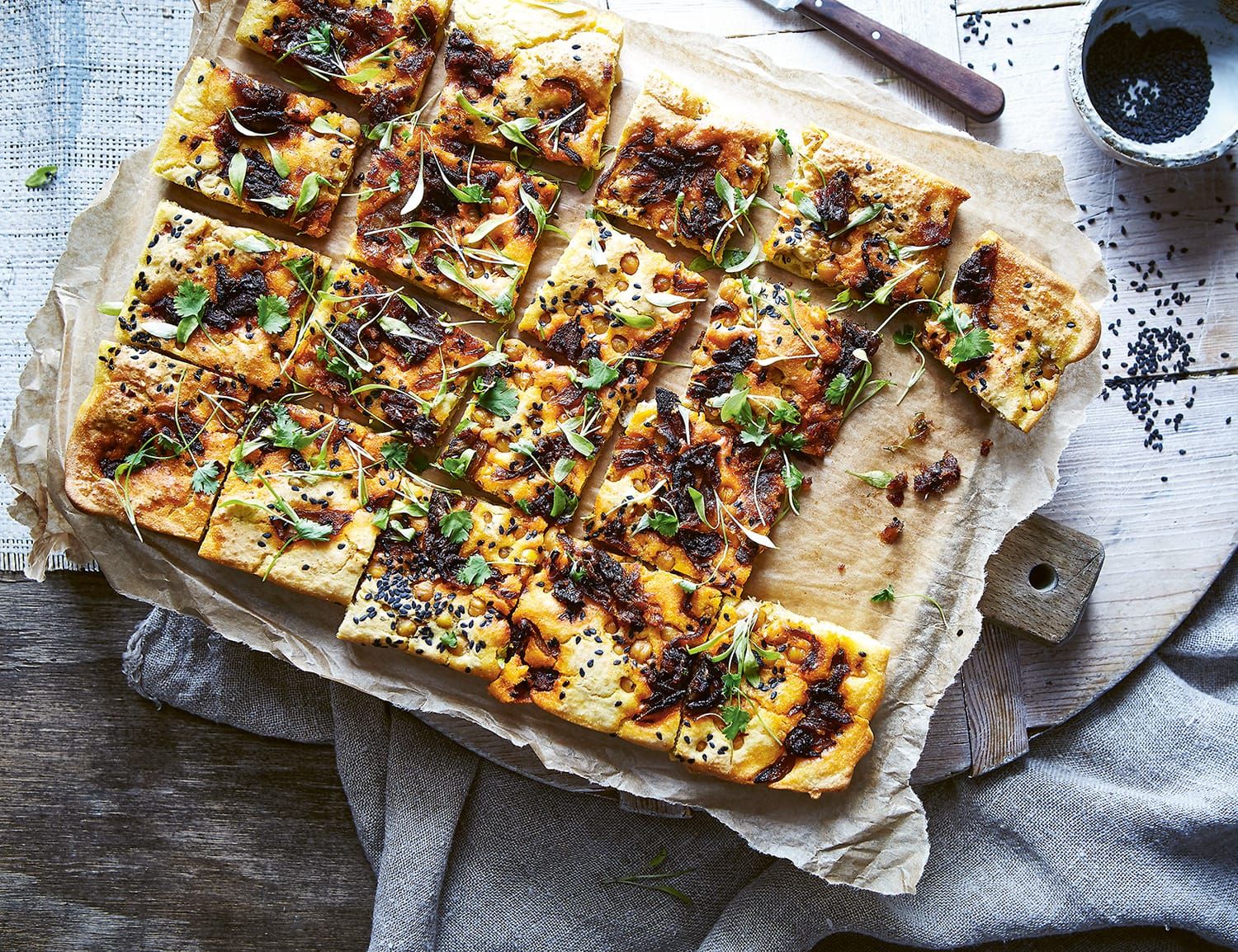 Photo of a tray of vegan, gluten-free chickpea flatbread, sprinkled with spices and herbs