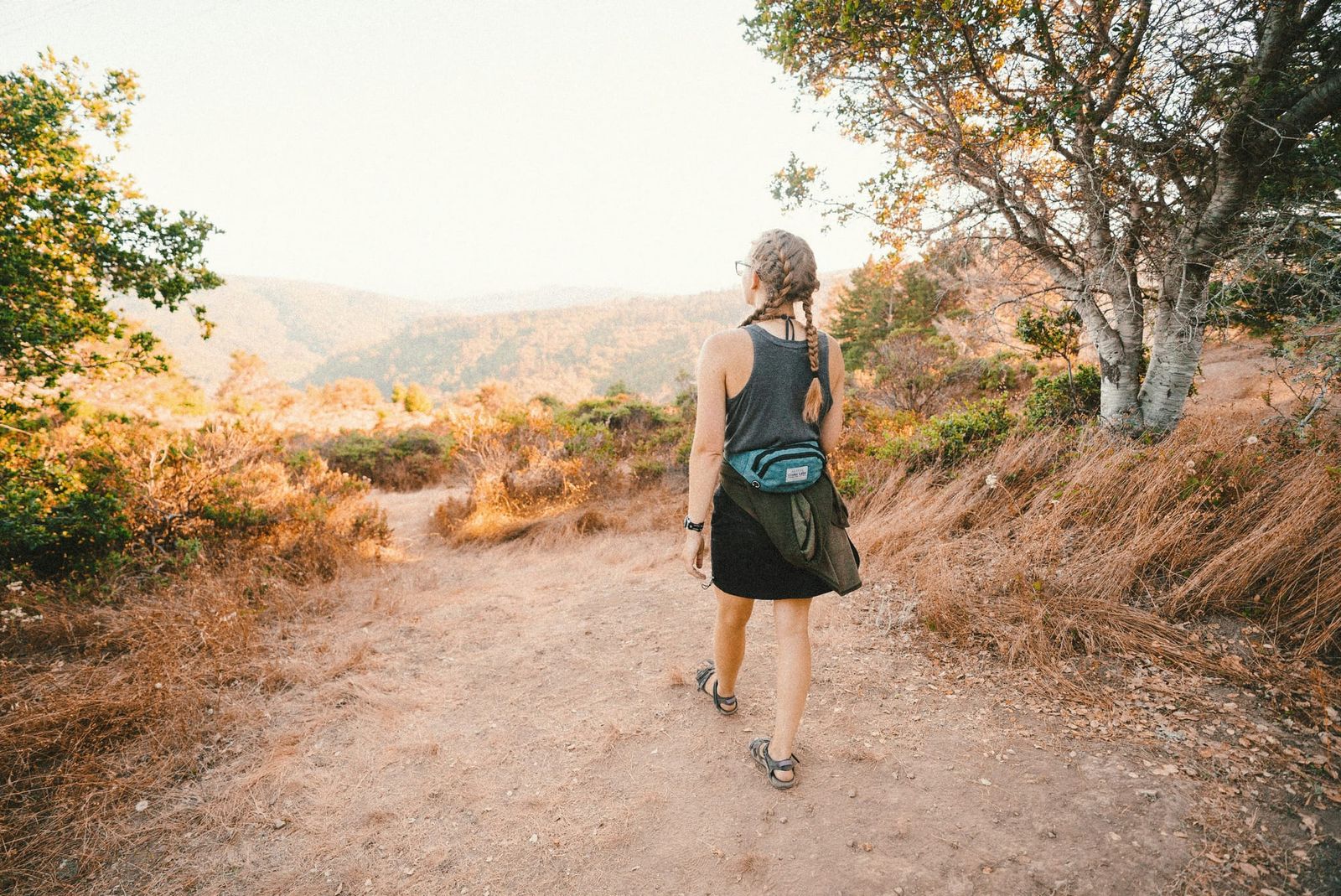 Photo shows a young person standing on a ledge, overlooking a valley, lit with sunlight