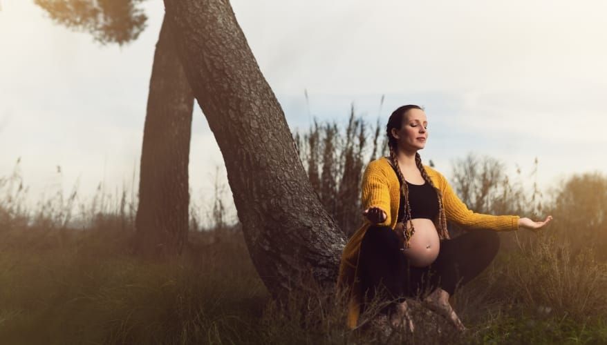 Photograph of a pregnant woman crouched by the trunk of a tree