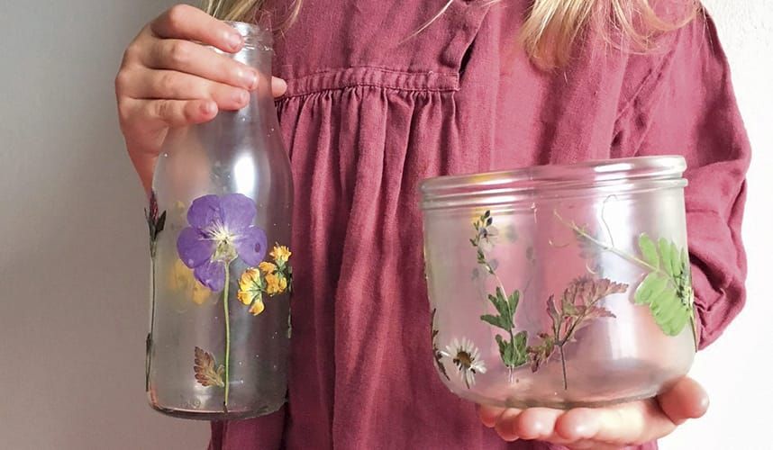 Photograph of a girl in a pink dress holding two recycled jam jars decorated with pressed flowers
