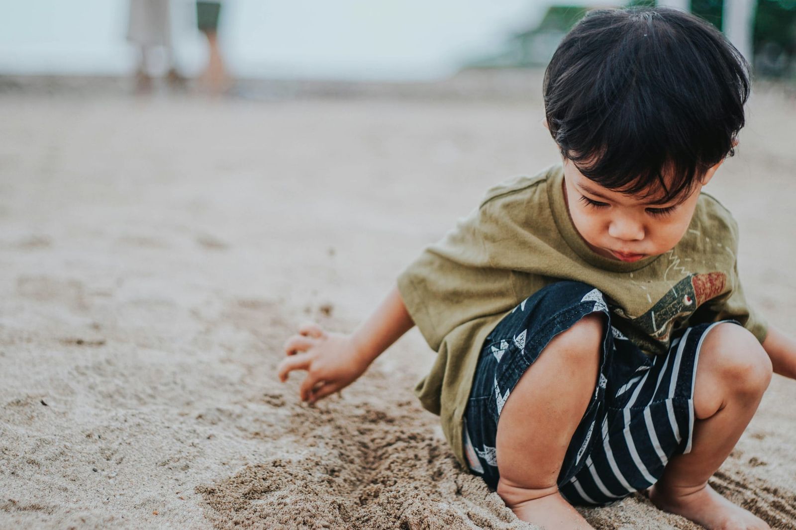 Photograph of a young child on a beach, playing in the sand and looking pensive