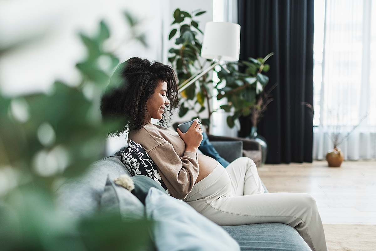 Photograph of a pregnant woman relaxing on a sofa with a cup of tea