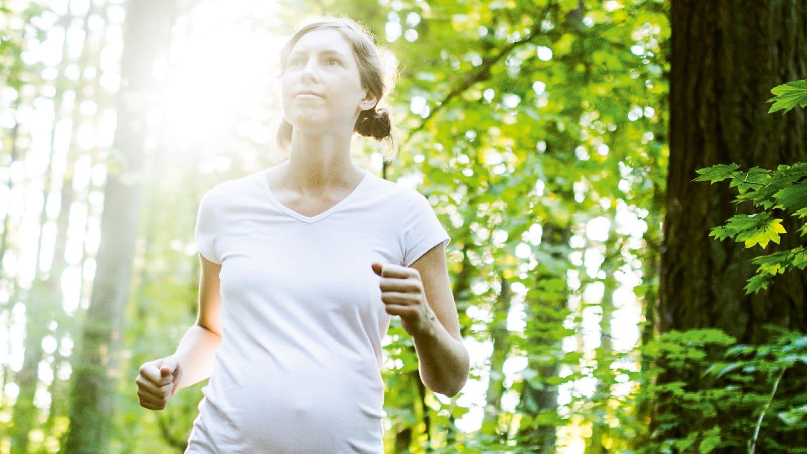 A pregnant woman running through a sunlit forest