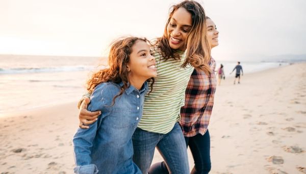 Mother walks along a sandy beach with her two teenage daughters
