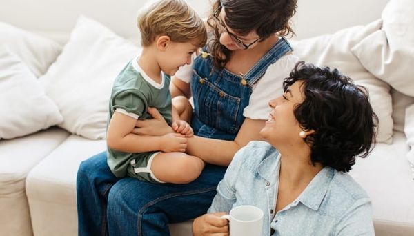 Two women sit on a sofa and the floor with their young son