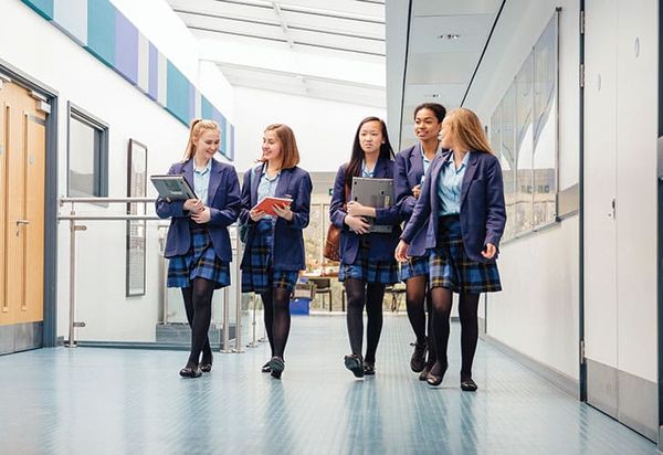 A group of school friends walk along a light, airy school corridor together