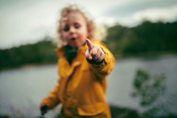 Photograph of a child in a yellow waterproof pointing at the camera