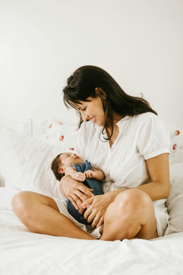 Mother sits on a bed, holding her tiny baby in her arms, gazing down at their face