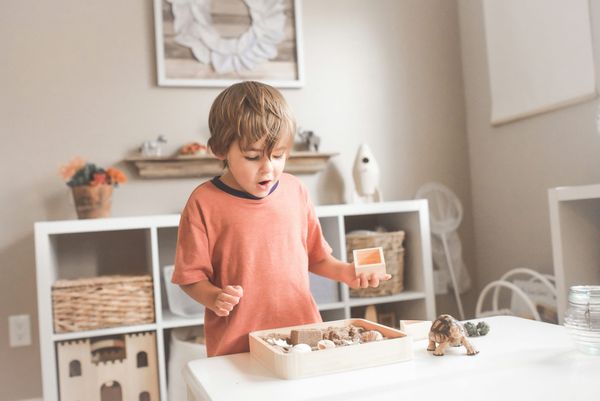 Photograph of a young child in a peach t-shirt standing by a table with some playthings