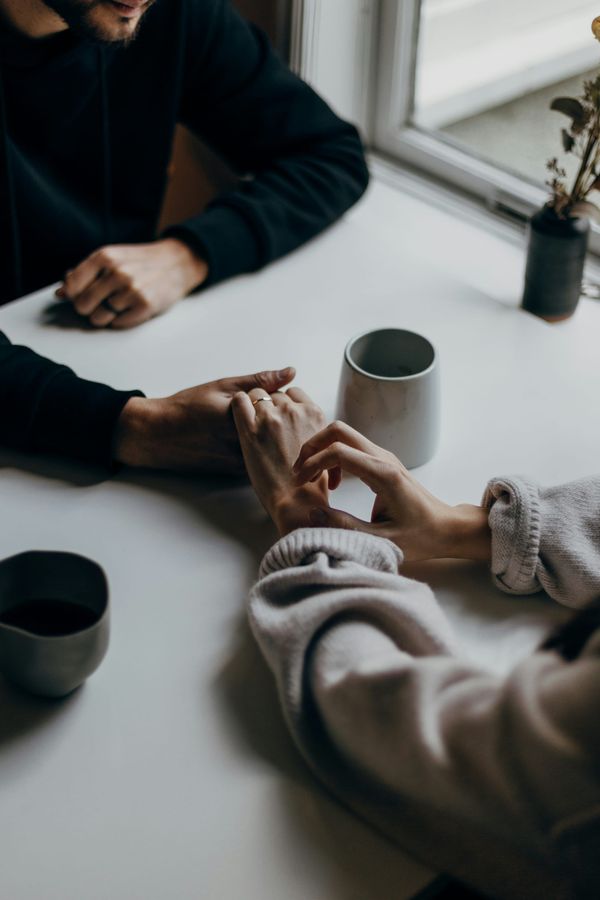 Couple hold hands over a table in a cafe, with a cup of coffee between them
