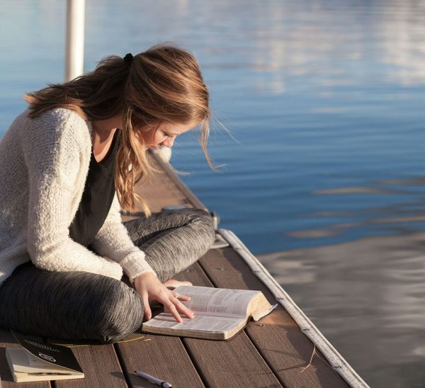 Photograph of a woman on a jetty reading a book