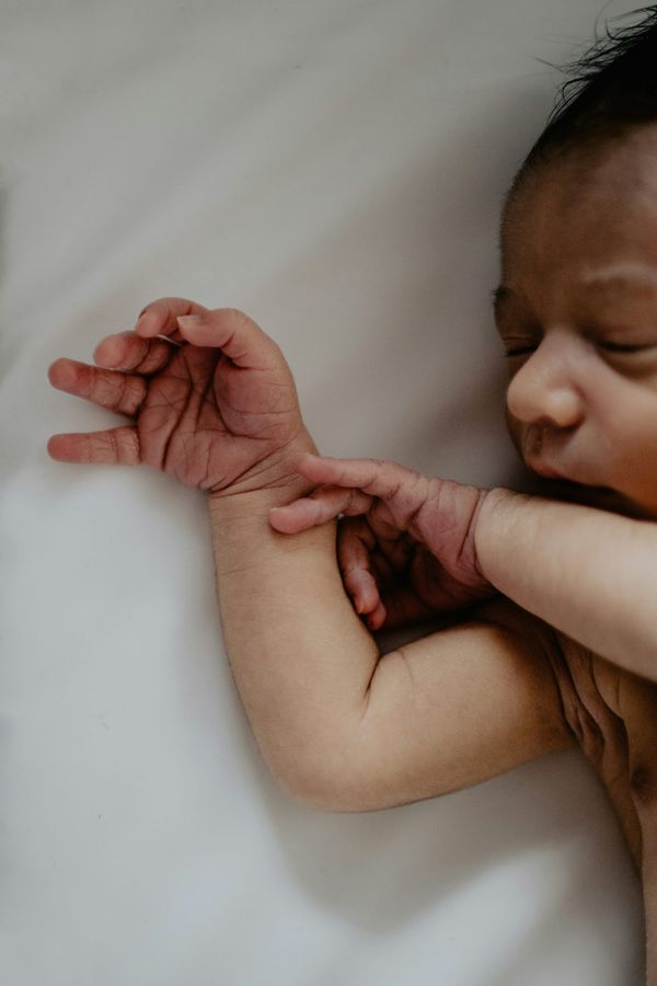 Photo of a newborn baby lying on a white sheet, just upper part of body, mainly arms and hands shown