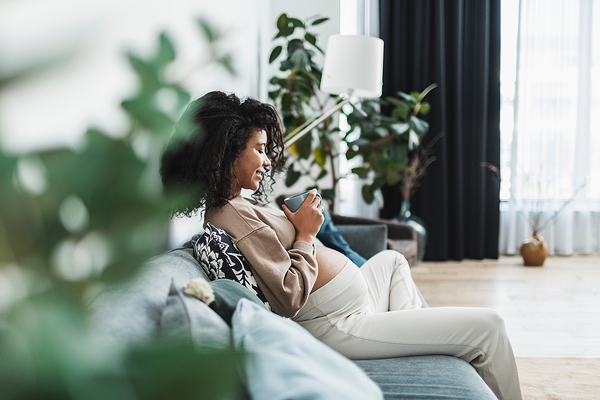 Photograph of a pregnant woman relaxing on a sofa with a cup of tea