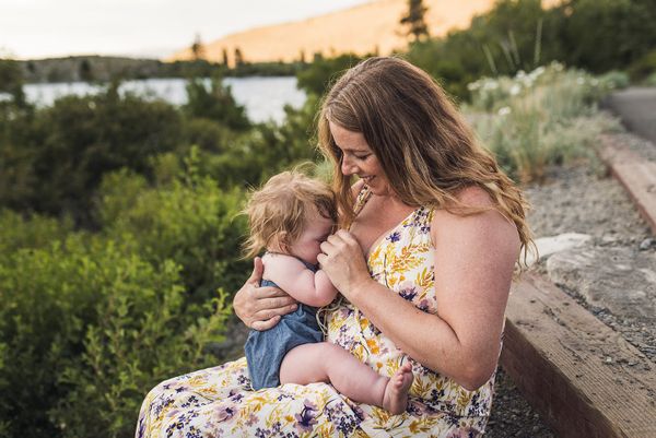 Mother sits in nature with a young child on her lap, breastfeeding