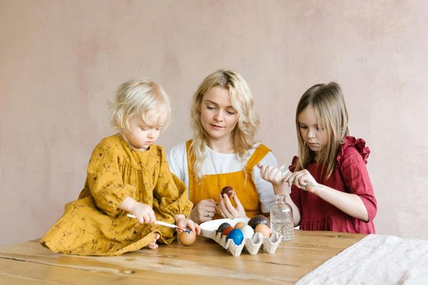 A Young Woman Beside a Baby Sitting on Table Painting an Egg