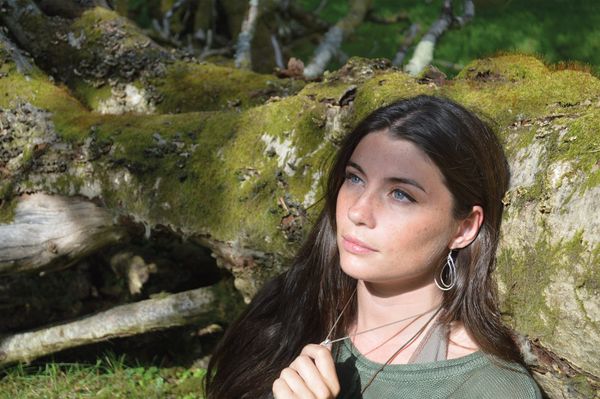 Seren Hawley-Plows sitting in the sunshine in front of a fallen, moss-covered tree trunk