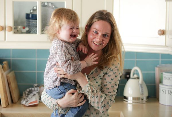 A smiling mother holding her crying toddler in the kitchen