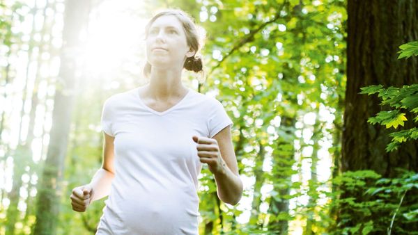 A pregnant woman running through a sunlit forest
