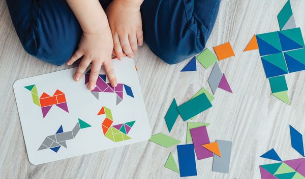 Child playing with colourful tangram pieces and pattern cards